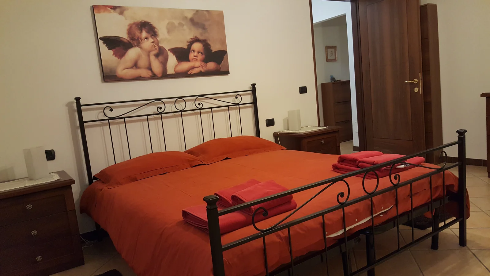 Camera matrimoniale con letto in ferro battuto e copriletto terracotta